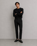 Hombre con pantalones de vestir negros Mildnight Milano de The Picks Club, jersey negro y mocasines de cuero